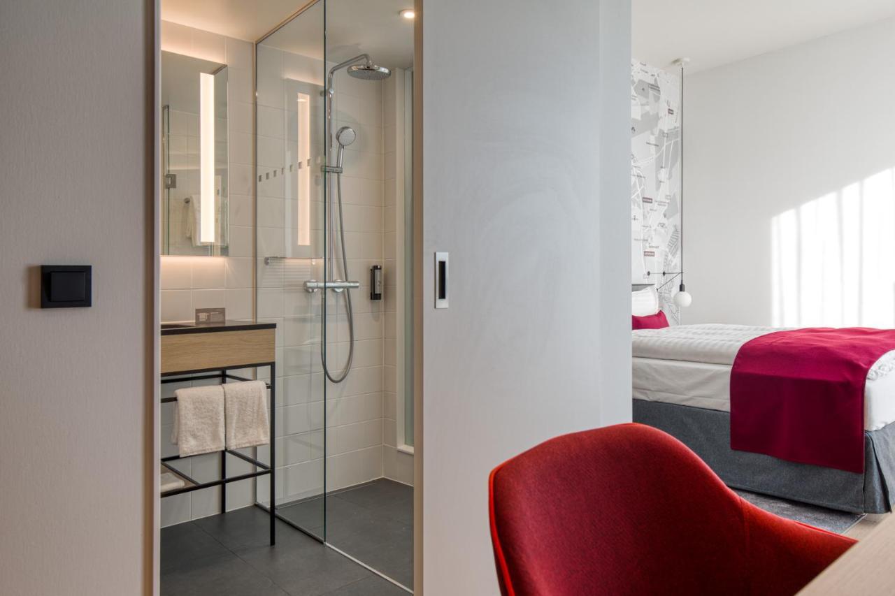 Intercityhotel Berlin Airport Ber Terminal 1 & 2 Шёнефельд Экстерьер фото The photo shows a modern hotel room or bathroom space. On the left, there is a glass-enclosed shower area with a sleek design, featuring a showerhead and minimalist fixtures. Adjacent to the shower, there's a sink area with a stylish countertop and a